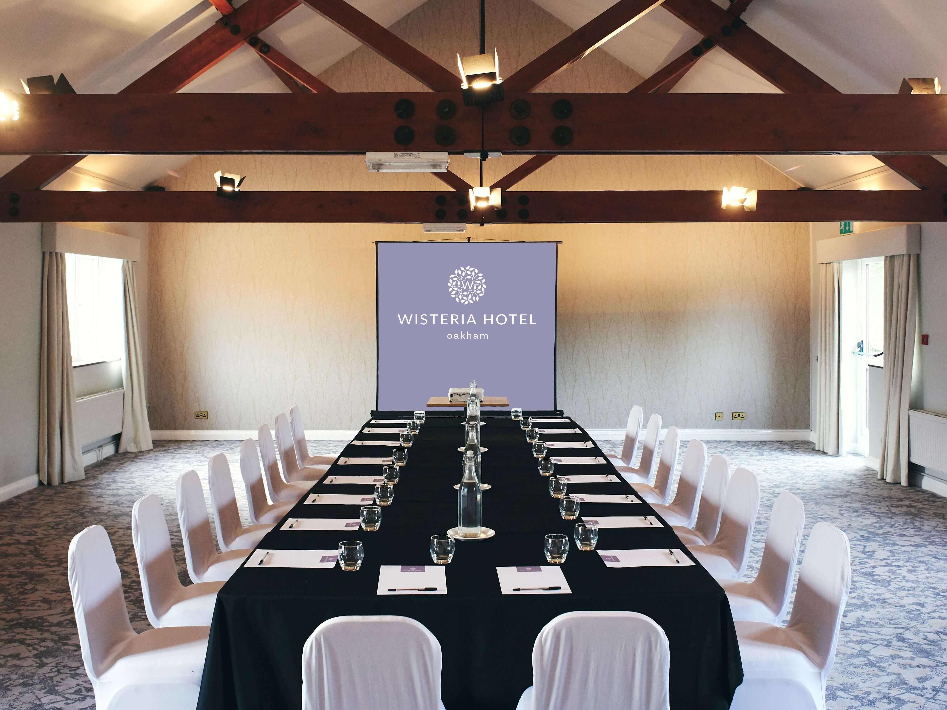 Conference room setup at Wisteria Hotel Oakham with long table, white chairs, and projector screen
