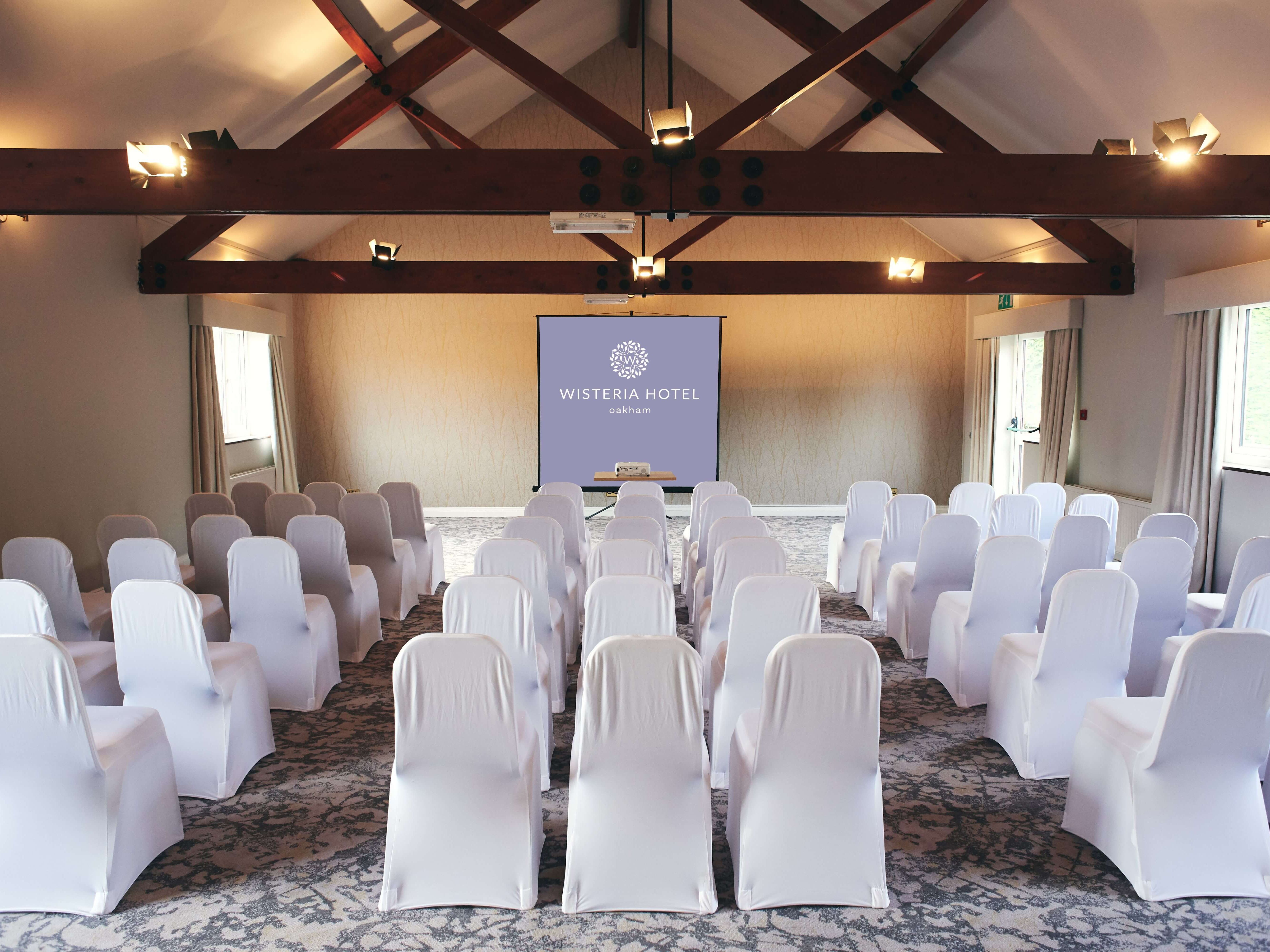 Conference or meeting room at Wisteria Hotel Oakham with rows of white covered chairs facing a projector screen.