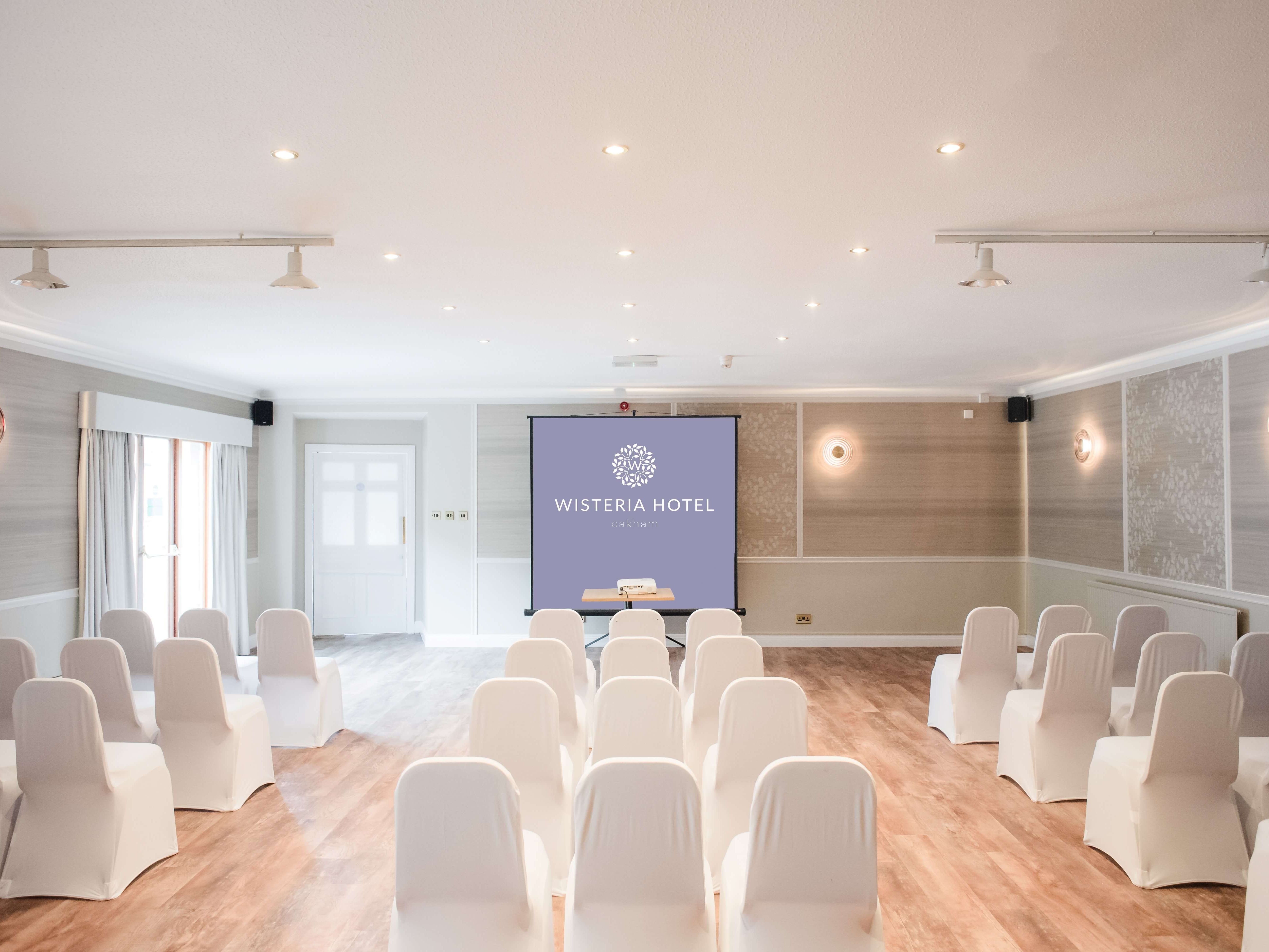Conference room at Wisteria Hotel set up with white chairs facing a projection screen.