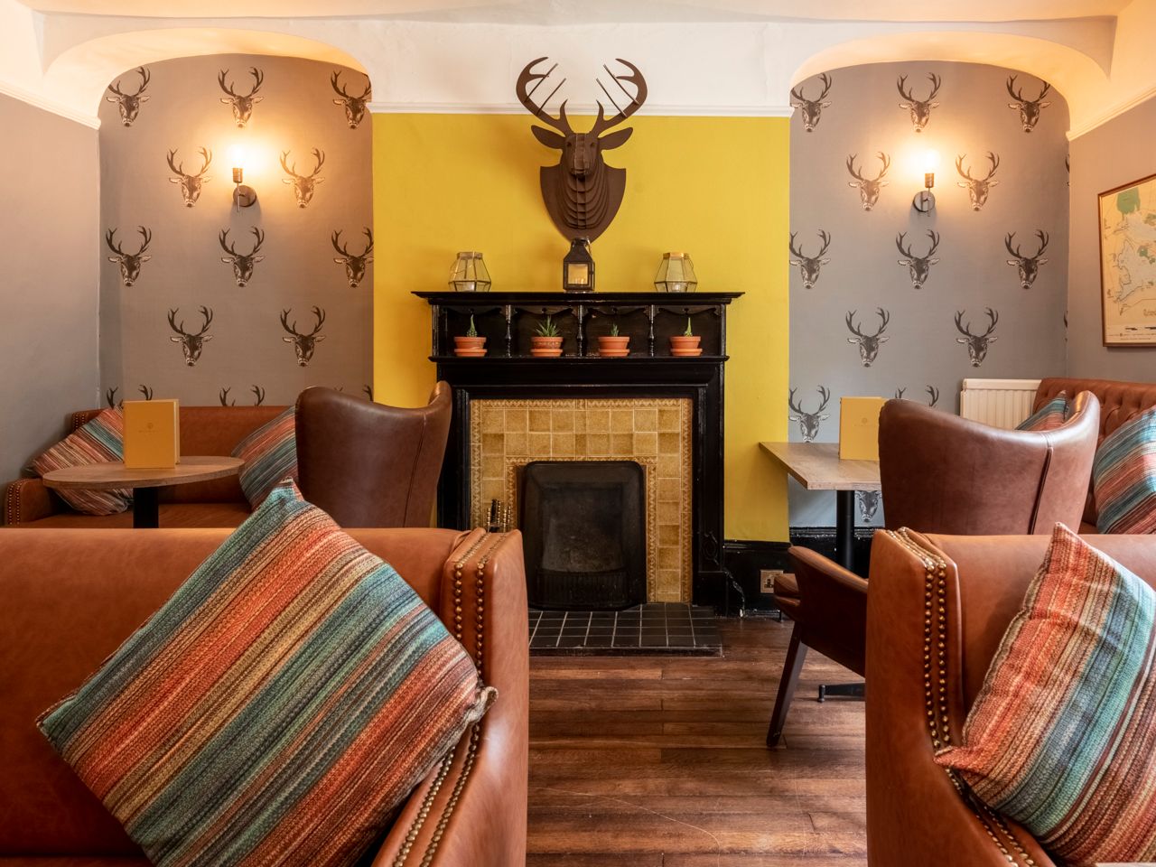 Cozy sitting area with leather chairs, striped pillows, a fireplace, and deer head wallpaper
