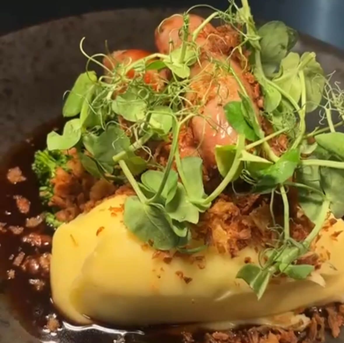 Gourmet dish with mashed potatoes, vegetables, fried onions, greens, and sauce