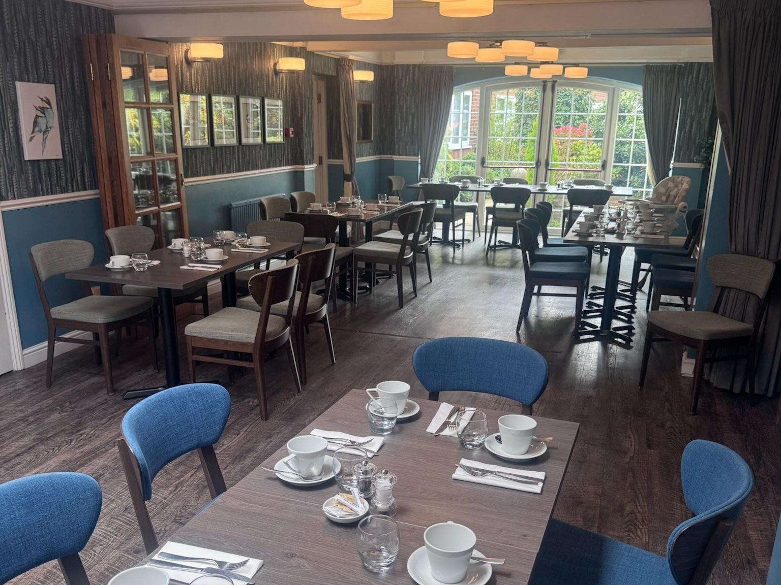 Elegant restaurant dining room with wooden tables and blue chairs set for a meal.