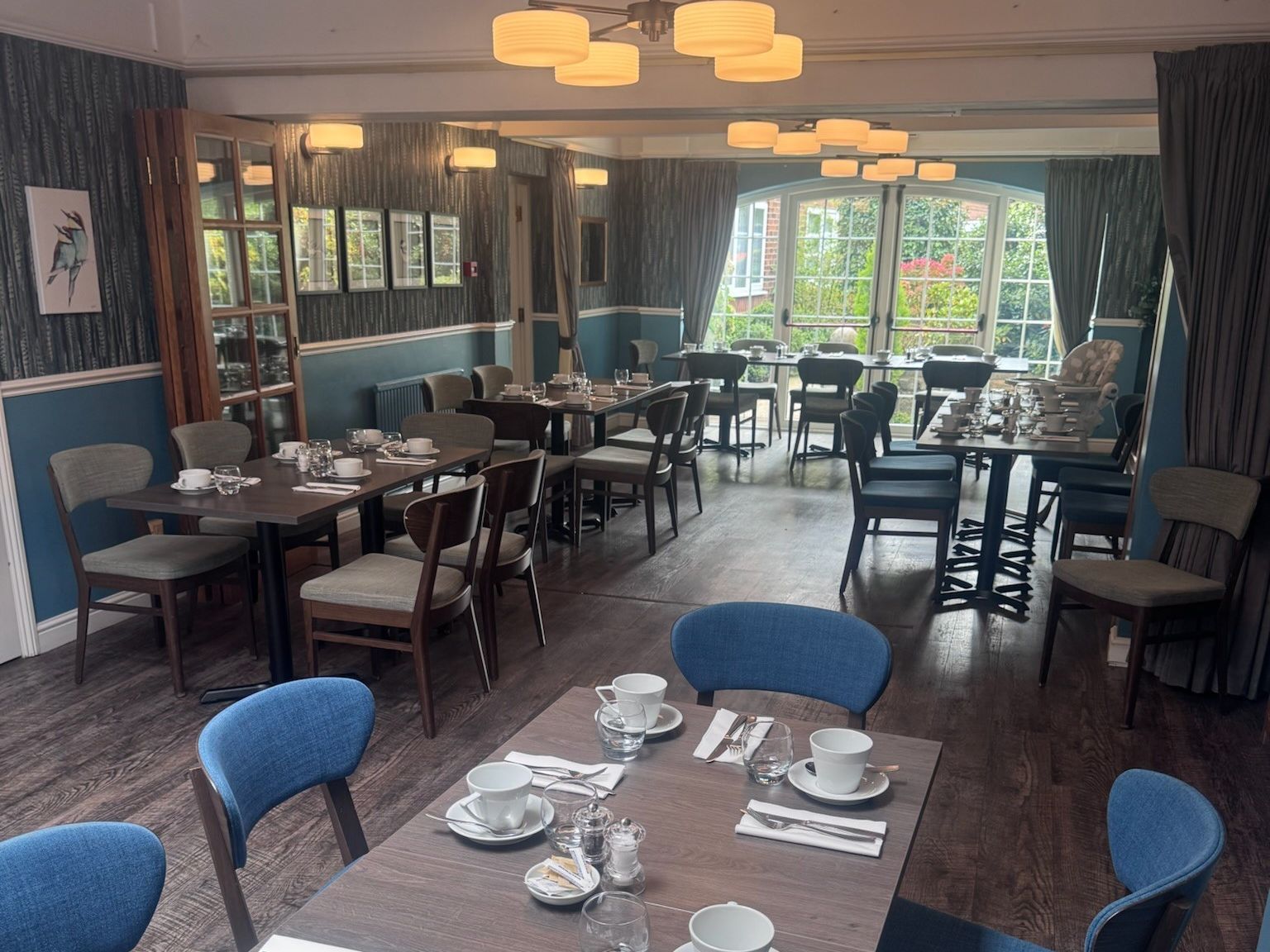 Elegant restaurant dining room with wooden tables and blue chairs set for a meal.