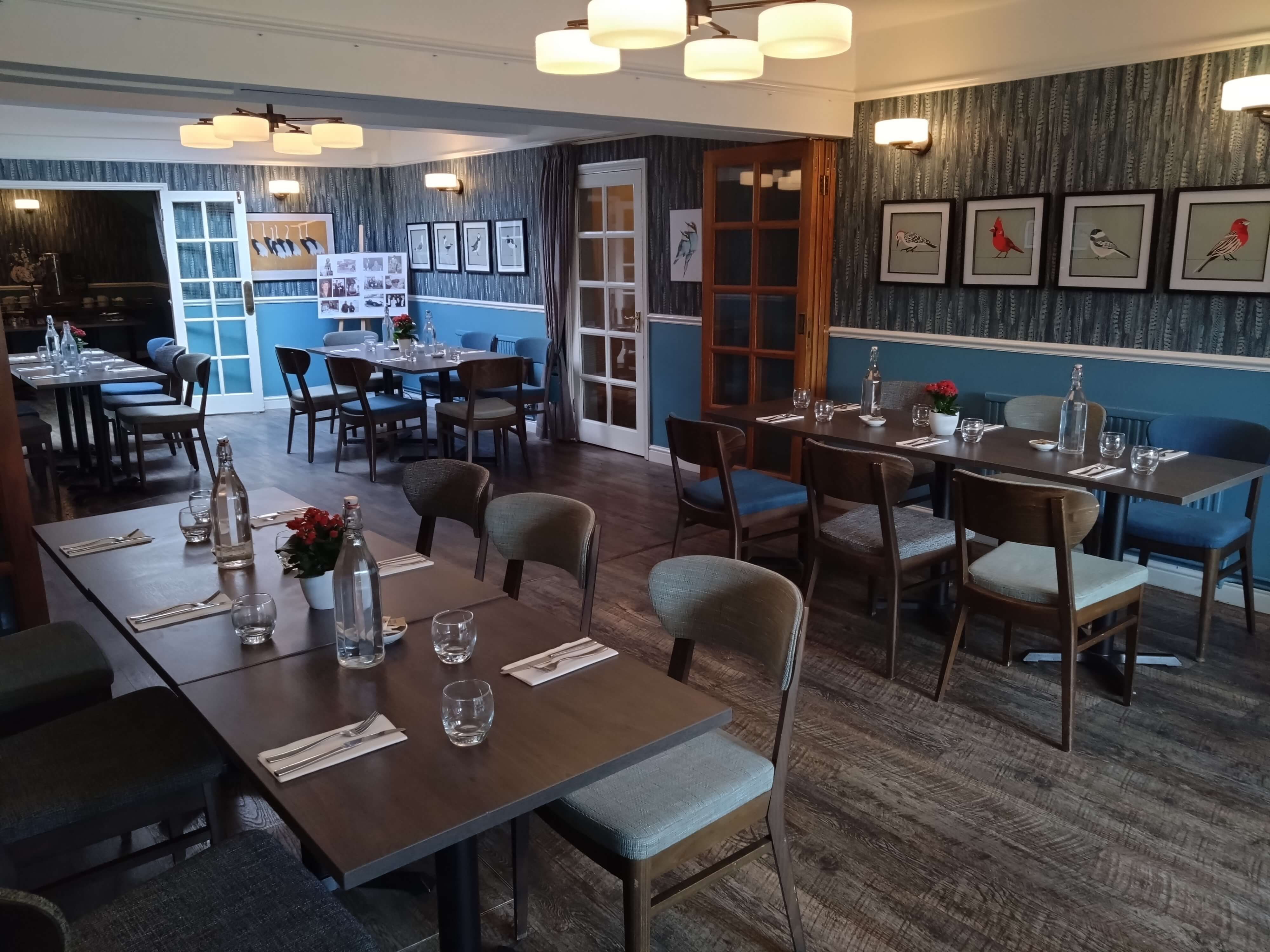 A modern dining room with several tables and chairs, decorated with bird artwork on the wall.