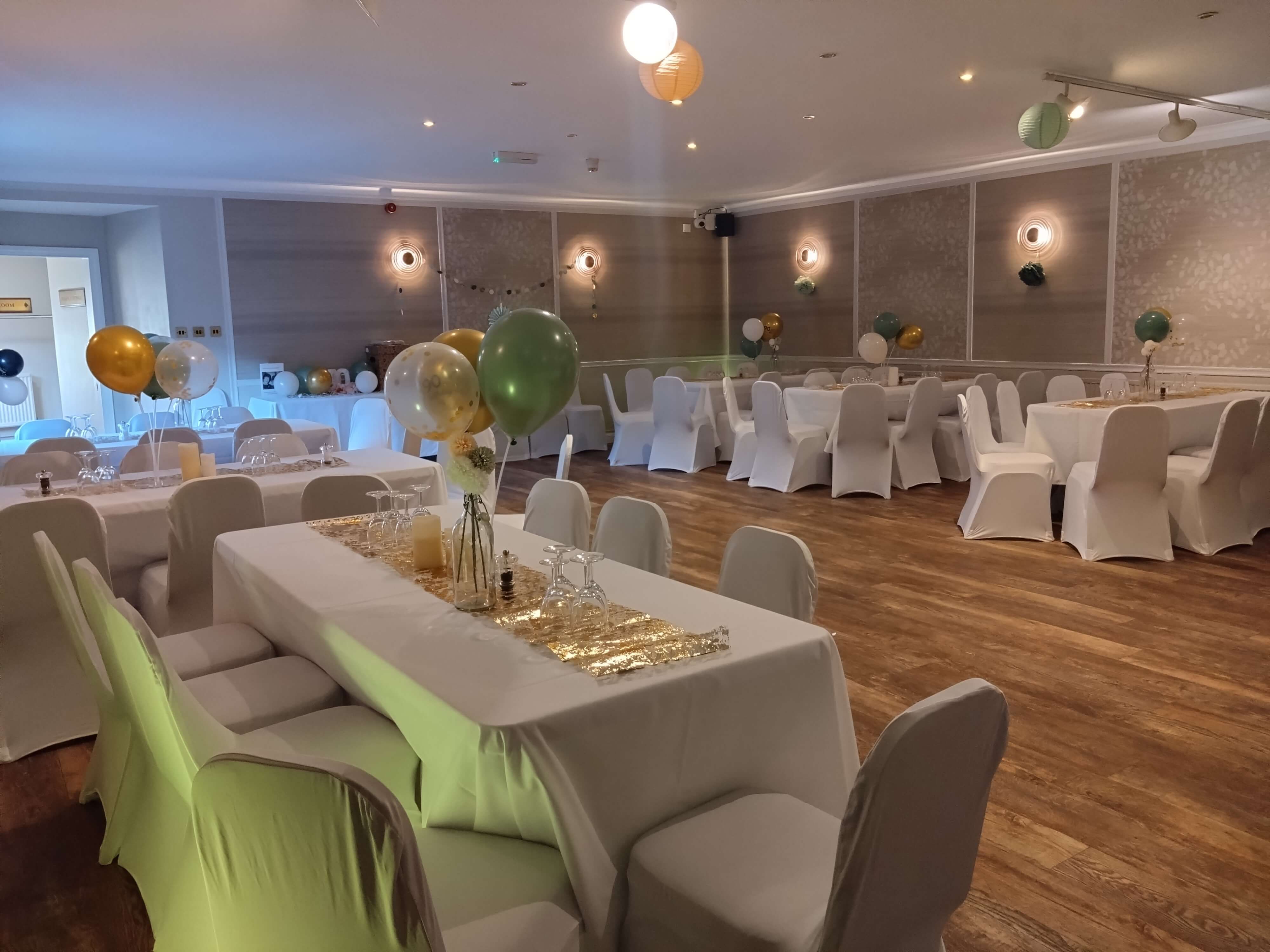 Elegant banquet hall with decorated tables, white chair covers, and colorful balloons