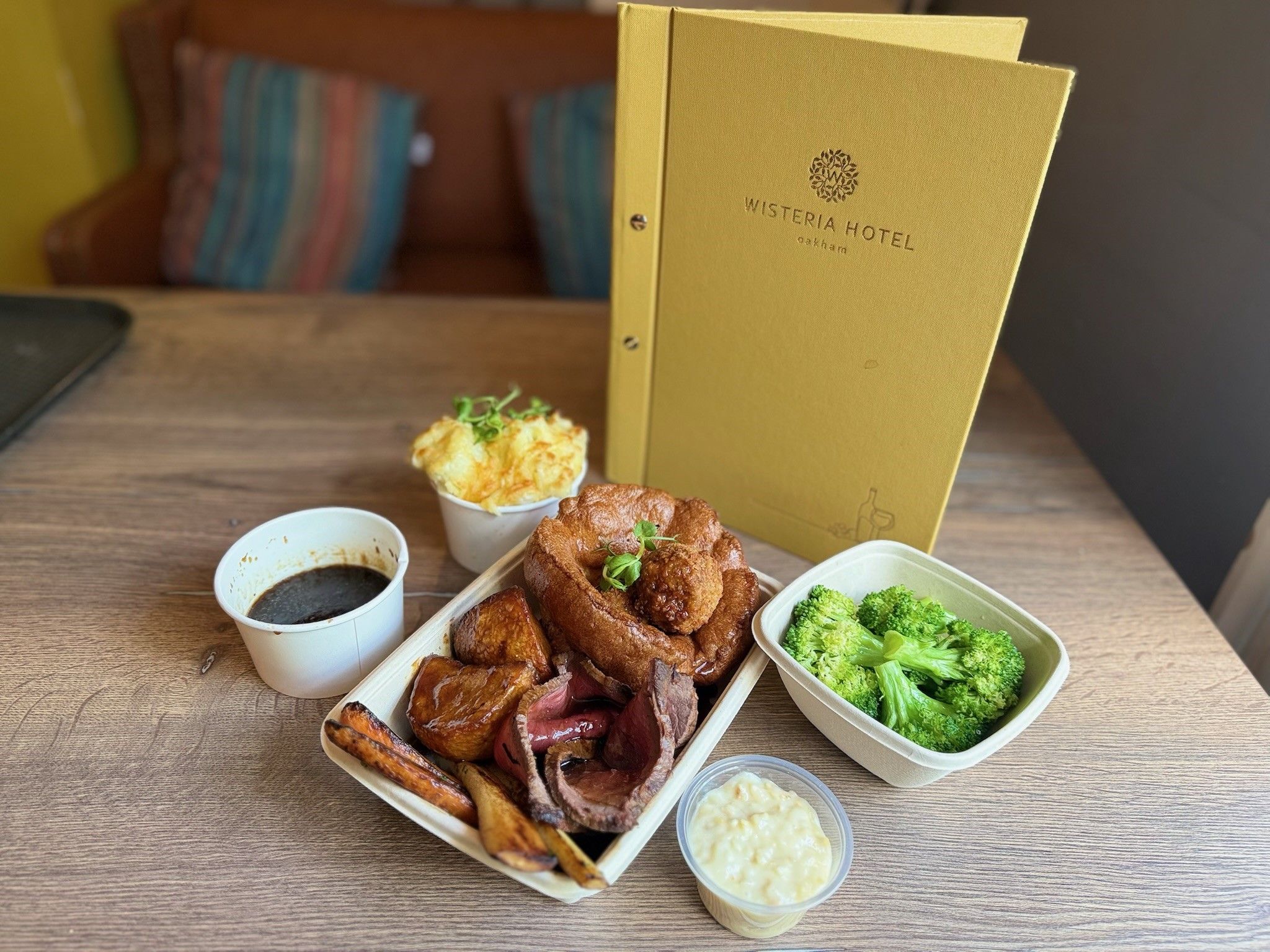 Traditional roast dinner with beef, vegetables, Yorkshire pudding, gravy, and sides, next to Wisteria Hotel menu on a table.
