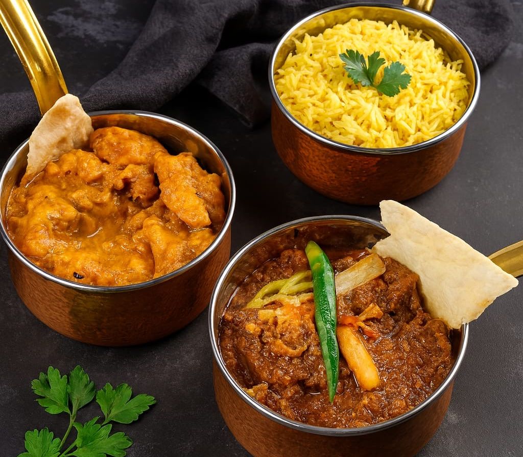 Indian curry dishes served in copper bowls with rice and naan
