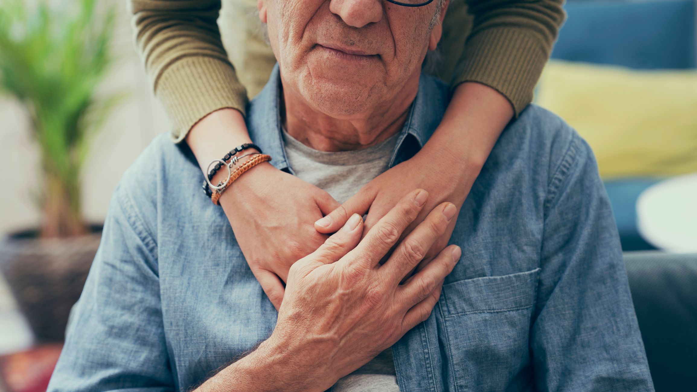 Close-up of an elderly man being gently embraced from behind by a younger person, symbolising support and compassion in dementia care.