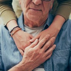 Close-up of an elderly man being gently embraced from behind by a younger person, symbolising support and compassion in dementia care.