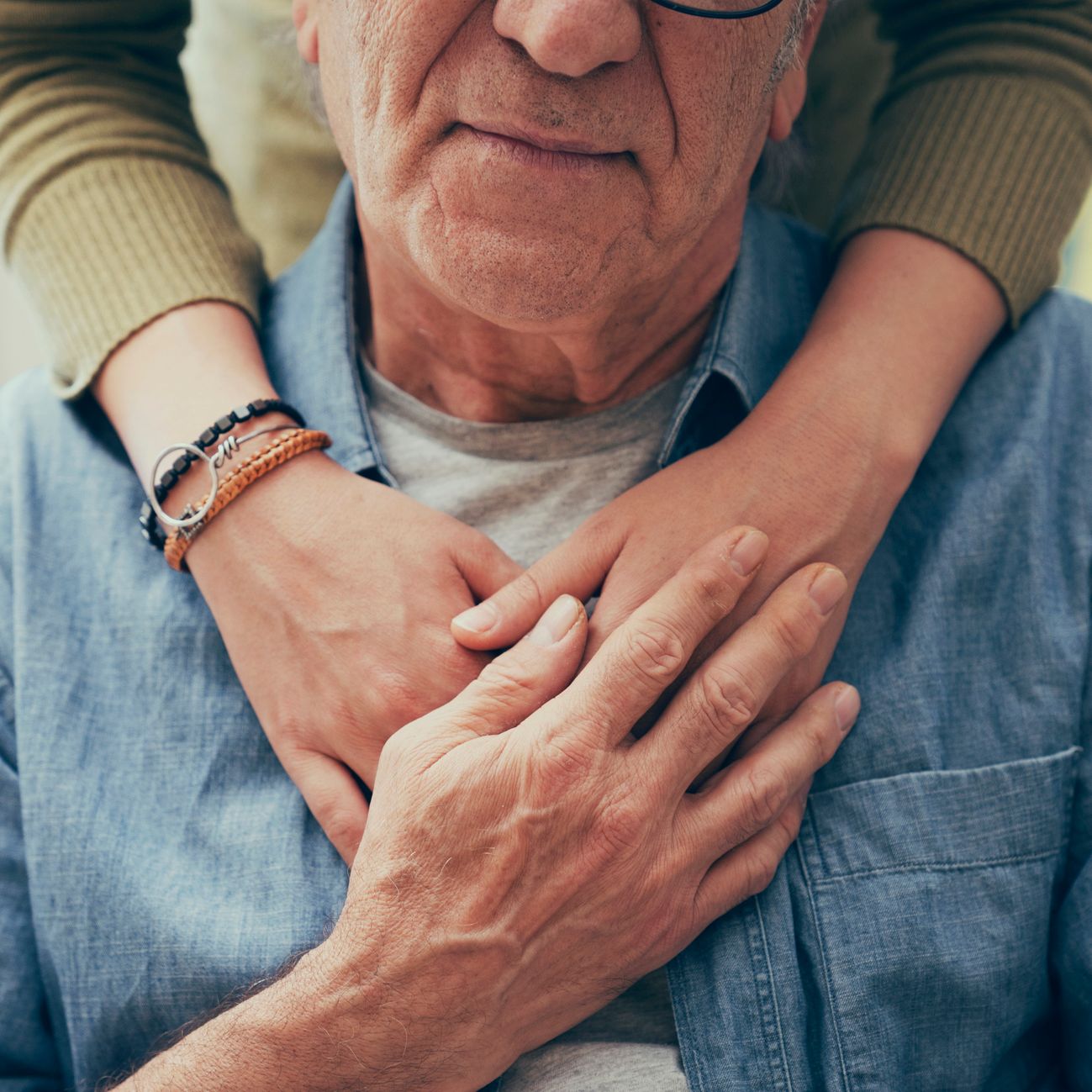 Close-up of an elderly man being gently embraced from behind by a younger person, symbolising support and compassion in dementia care.