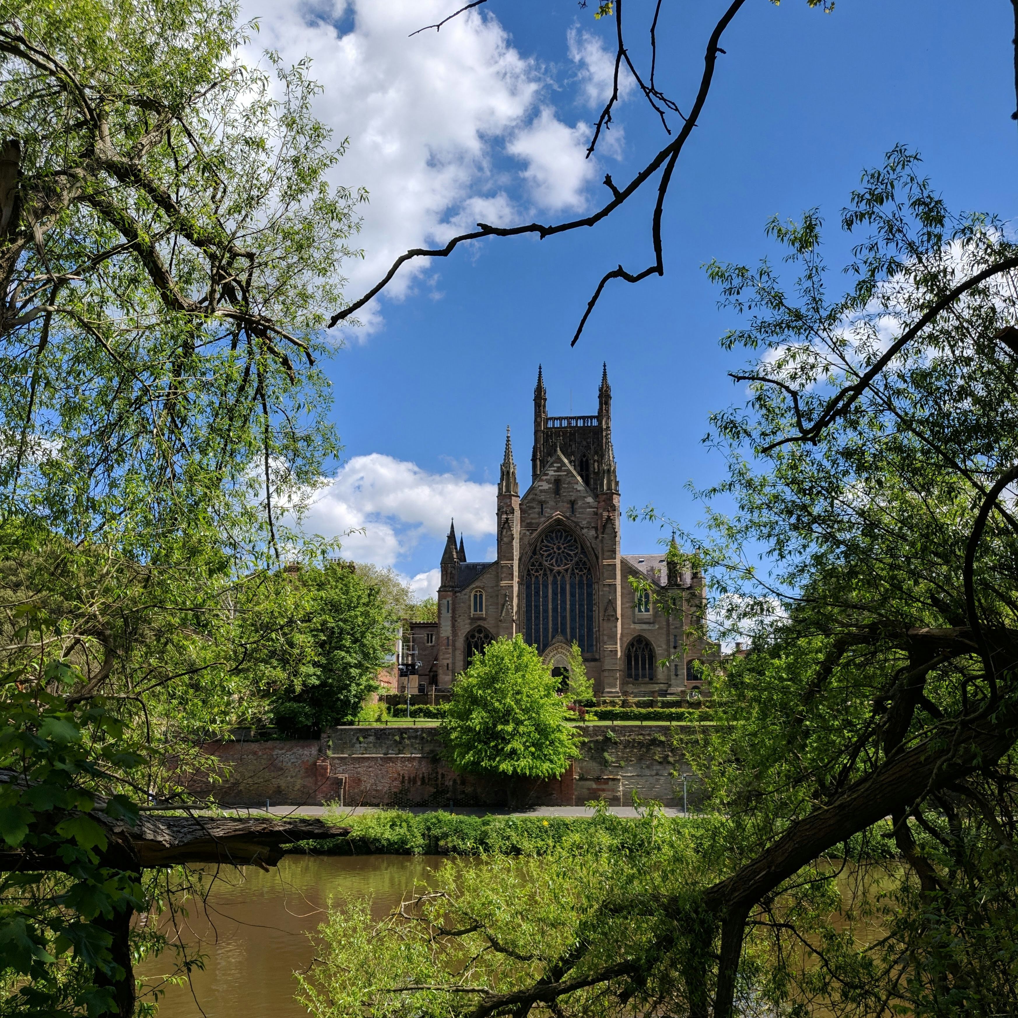 Worcester Cathedral viewed through trees from across the River Severn on a sunny day