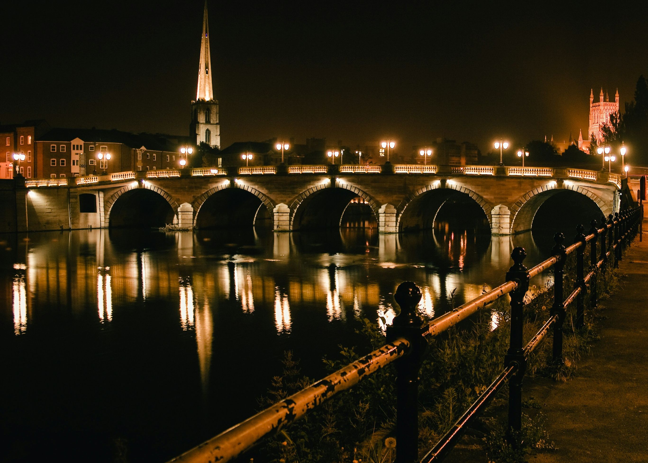 Worcester bridge and riverside lit up at night with reflections on the River Severn and cathedral in the background