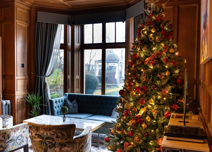 Elegant living room decorated for Christmas with a lit Christmas tree and cozy seating by a large window.