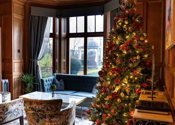 Elegant living room decorated for Christmas with a lit Christmas tree and cozy seating by a large window.
