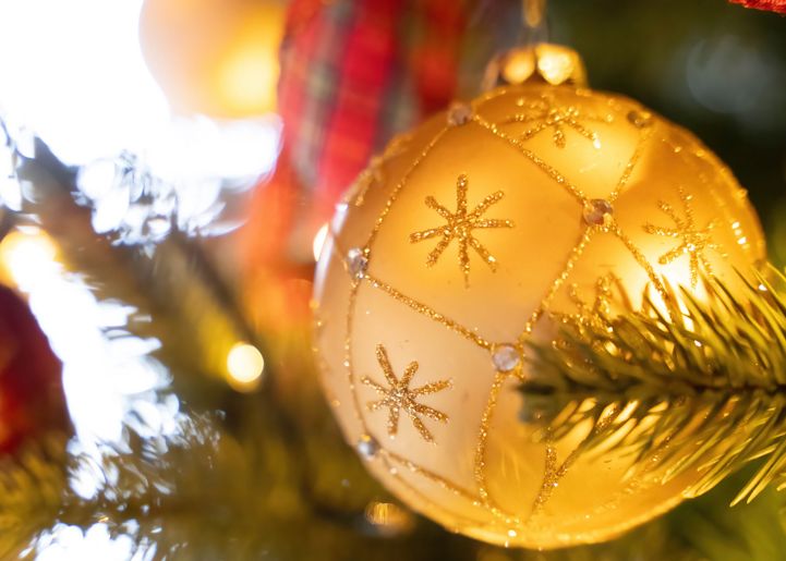 Close-up of a gold Christmas ornament with glittery snowflake patterns hanging on a decorated Christmas tree.