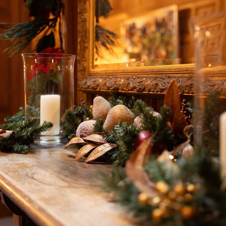 Christmas garland and candle decorations on a wooden mantel with a gold-framed mirror