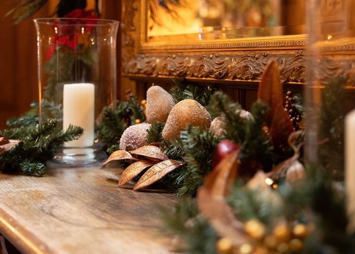 Christmas garland and candle decorations on a wooden mantel with a gold-framed mirror