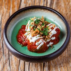 Bowl of meatballs topped with sauce, sour cream, crispy onions, and chopped herbs
