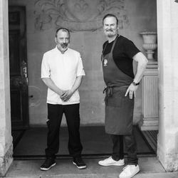 Two men in chef attire standing under an ornate archway