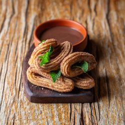 Churros served on a wooden board with chocolate dipping sauce and garnished with fresh mint leaves