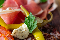 Close-up of assorted charcuterie meats, pickled pepper, marinated artichoke, and parsley garnish