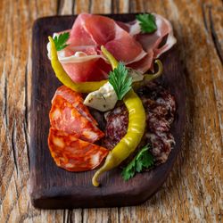 Charcuterie board with cured meats, peppers, and herbs on a wooden surface