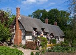 Traditional English cottage with thatched roof and brick chimneys surrounded by garden