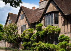Historic half-timbered building with leaded glass windows and a sloped tiled roof, surrounded by greenery.
