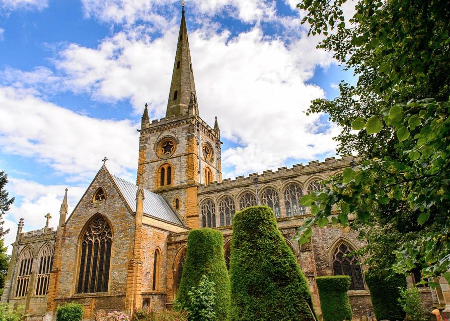 Holy Trinity Church: Shakespeare's Burial Site.Historic stone church with a tall spire and arched windows surrounded by greenery.