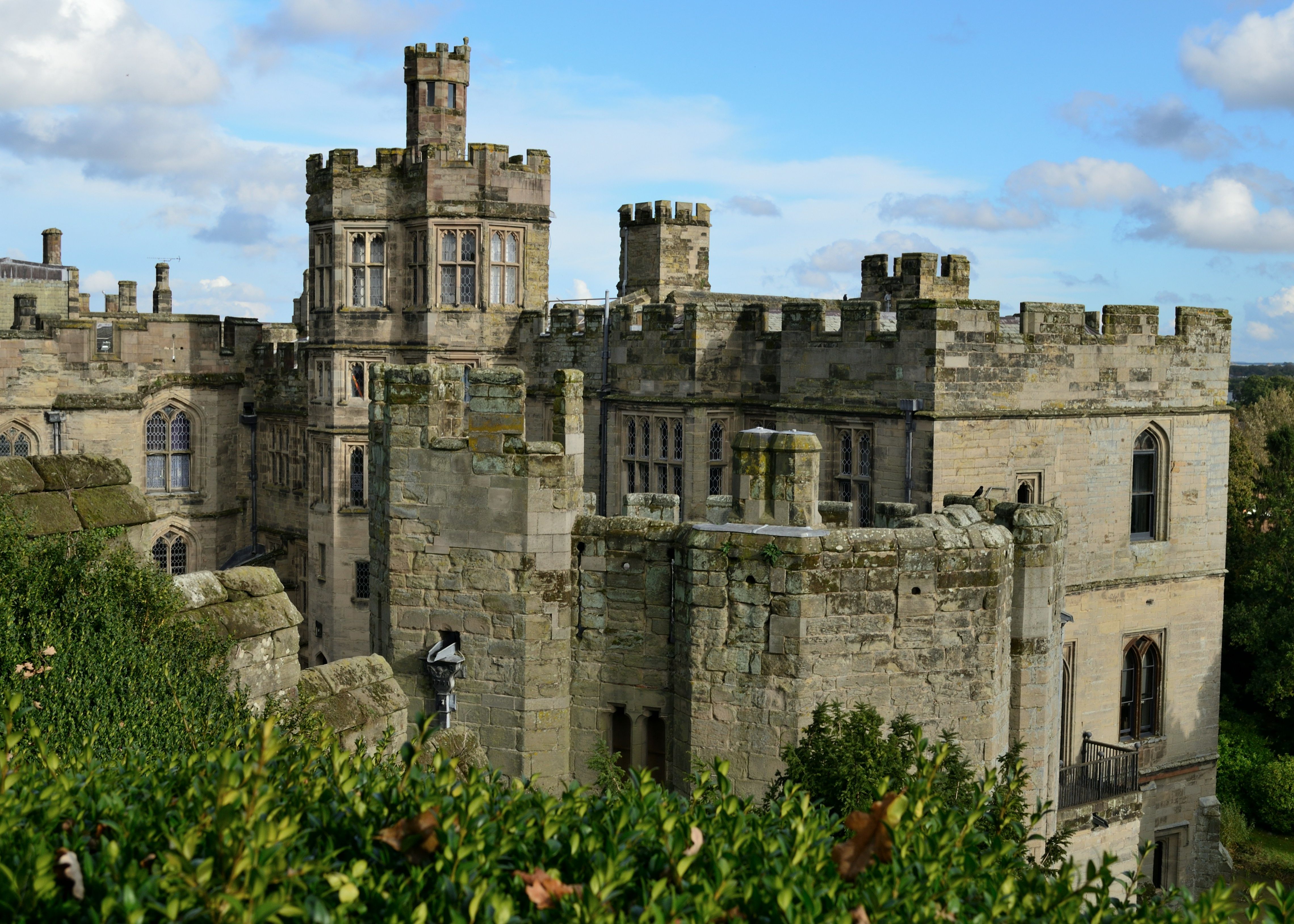 A medieval stone castle with crenellated towers and large windows under a blue sky.