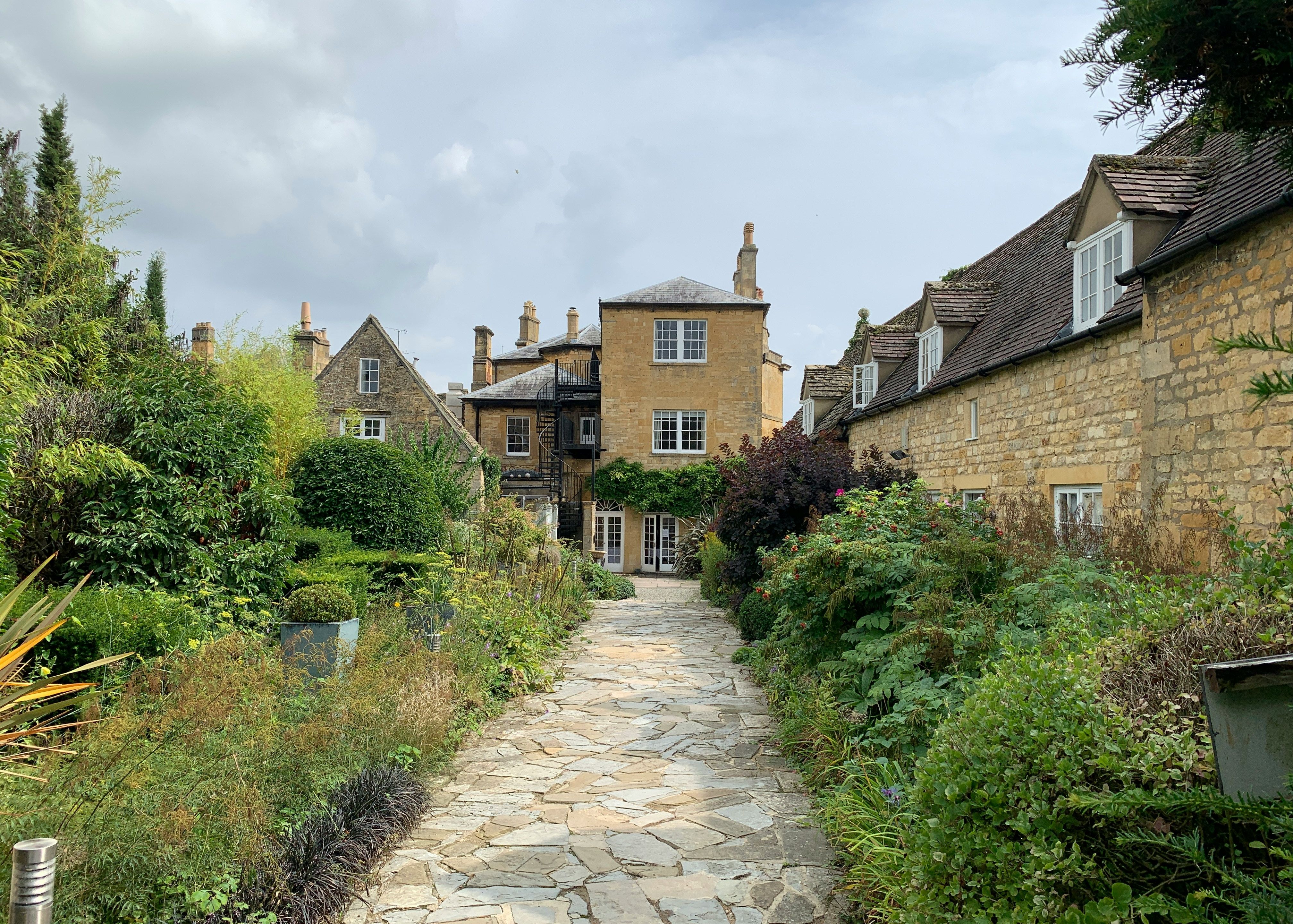 Stone path leading through a lush garden to traditional English stone houses.