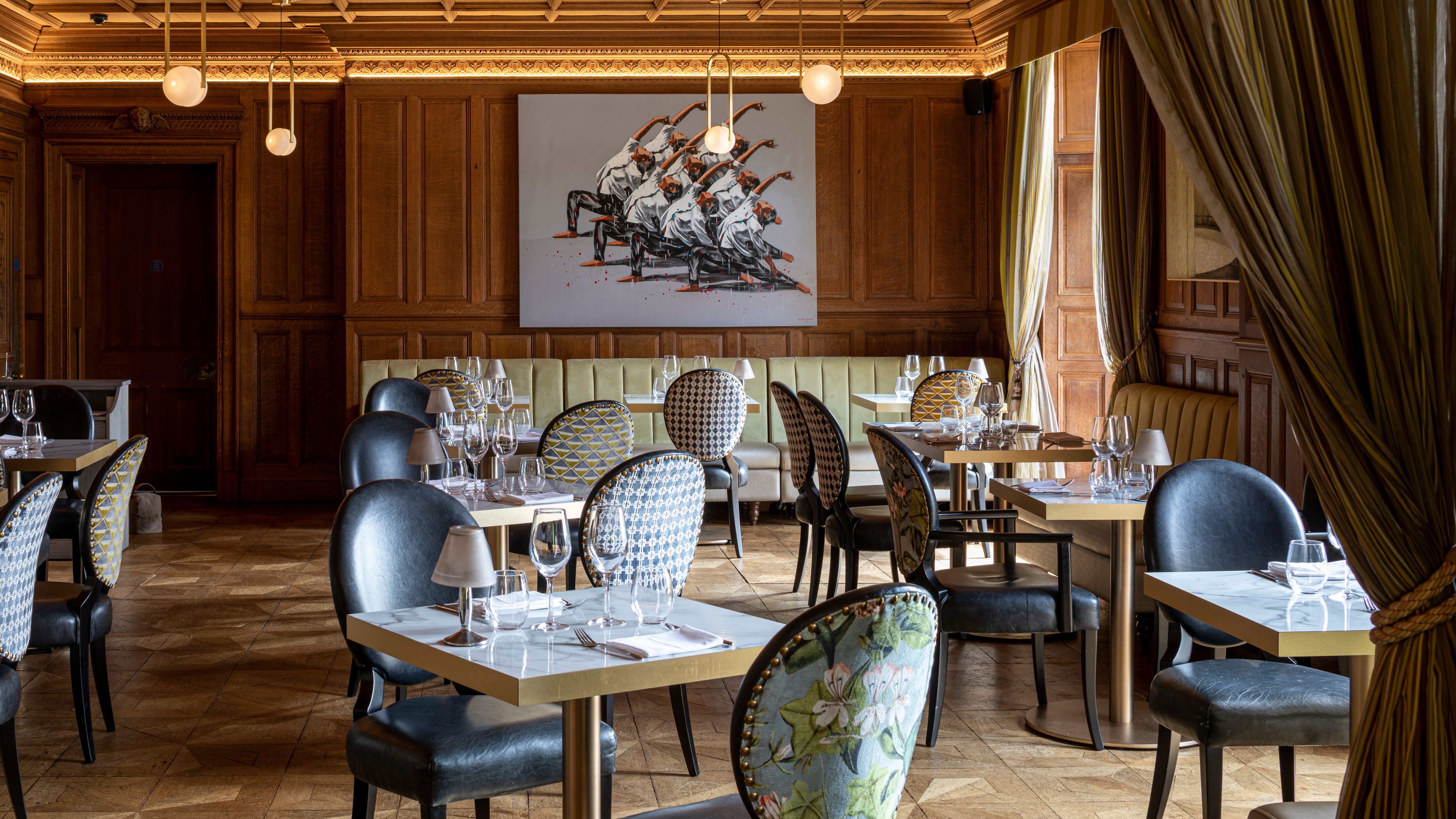 Elegant restaurant interior with patterned chairs, set tables, wooden paneling, and modern artwork on the wall.