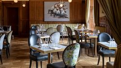Elegant restaurant interior with patterned chairs, set tables, wooden paneling, and modern artwork on the wall.