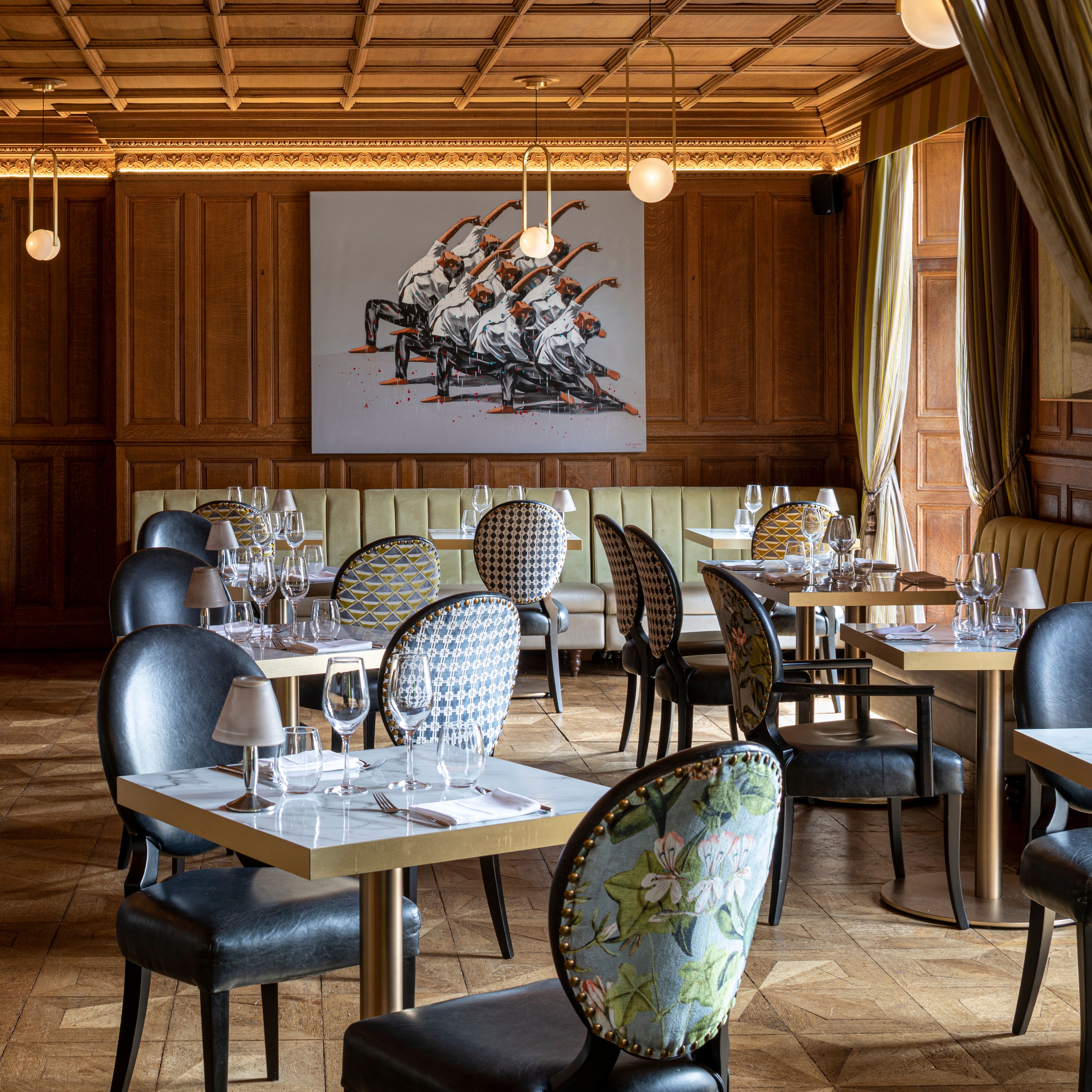 Elegant restaurant interior with patterned chairs, set tables, wooden paneling, and modern artwork on the wall.