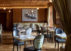 Elegant restaurant interior with patterned chairs, set tables, wooden paneling, and modern artwork on the wall.