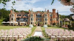 Outdoor wedding ceremony setup with rows of chairs, a decorated table, and a scenic manor house in the background.