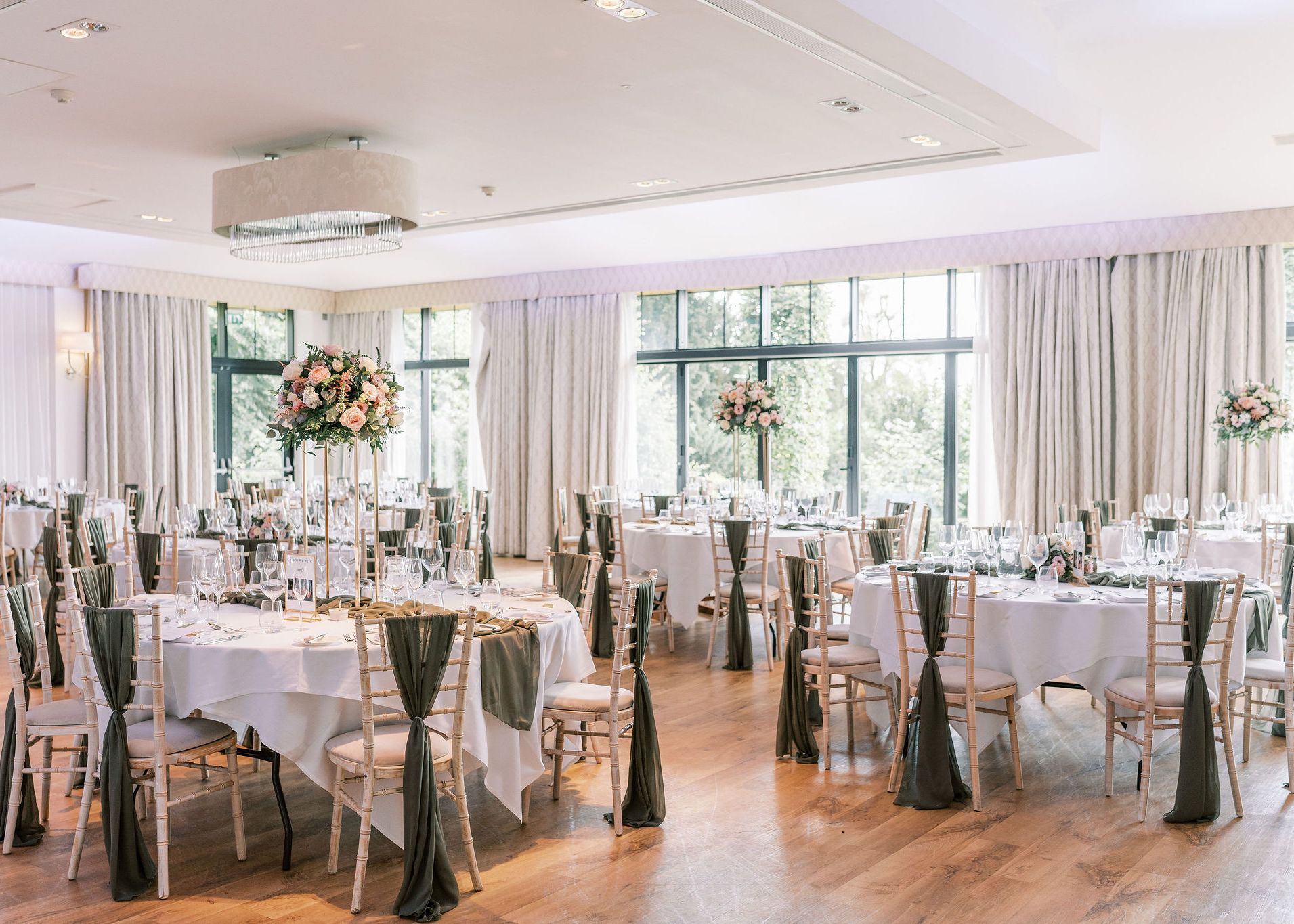 Elegant wedding reception setup with round tables, floral centerpieces, and floor-to-ceiling windows.