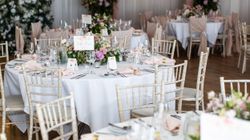 Elegant wedding reception setup with round tables, pink floral arrangements, and white chairs