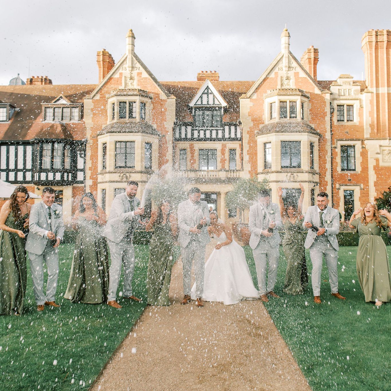 Wedding party celebrating with champagne in front of a large historic manor house