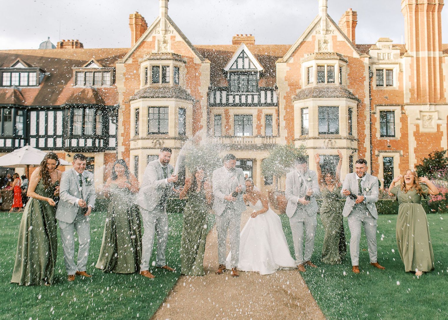Wedding party celebrating with champagne in front of a large historic manor house