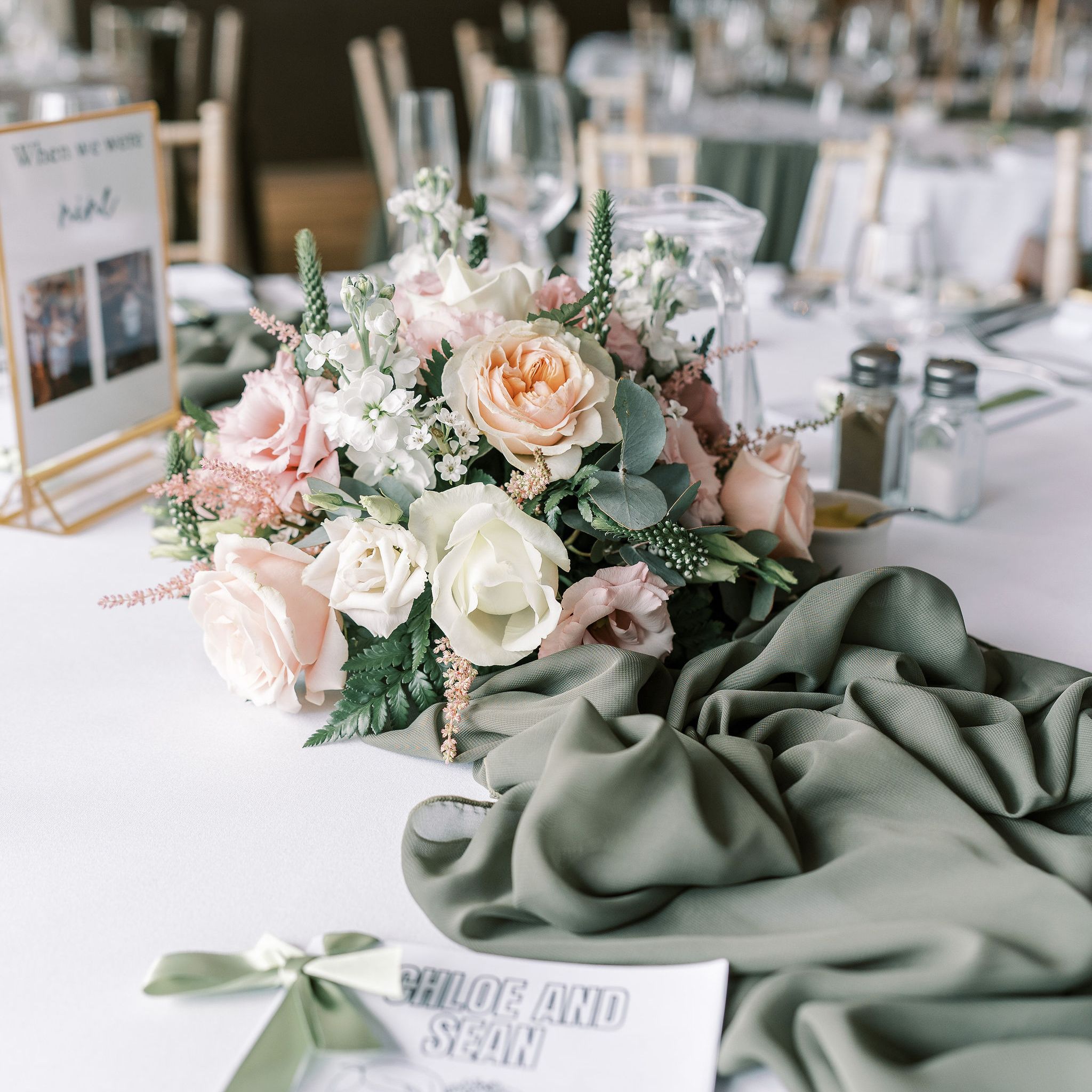 Elegant wedding table decorated with pastel flower arrangement, green table runner, and personalized coloring book for Chloe and Sean.