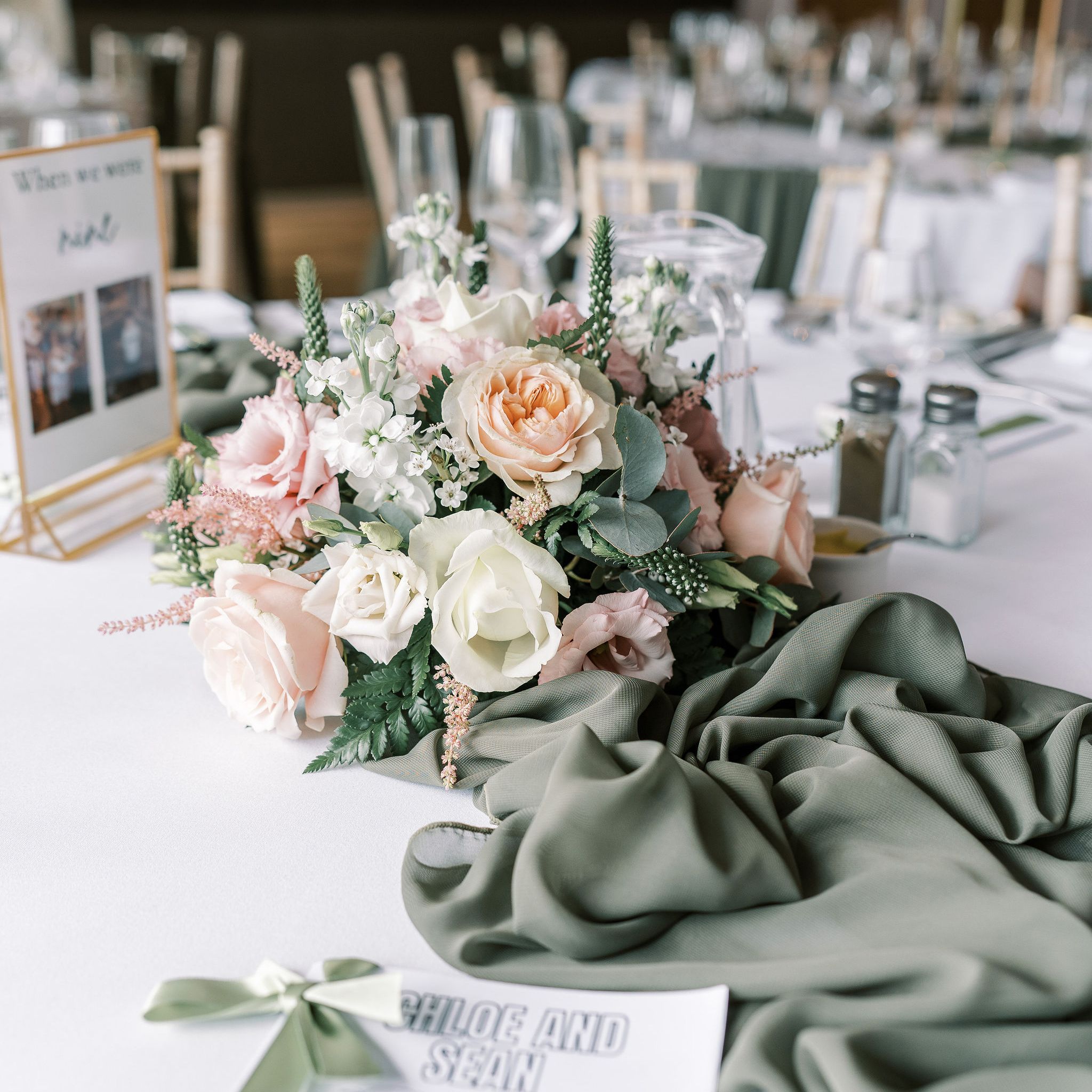 Elegant wedding table decorated with pastel flower arrangement, green table runner, and personalized coloring book for Chloe and Sean.