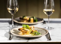 A gourmet meal plated with greens and grilled vegetables, served with white wine on a marble table.
