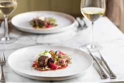 A gourmet plated dish with various colorful ingredients beside a glass of white wine on a marble table.