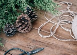 Pinecones, evergreen branches, twine, and scissors on a wooden table