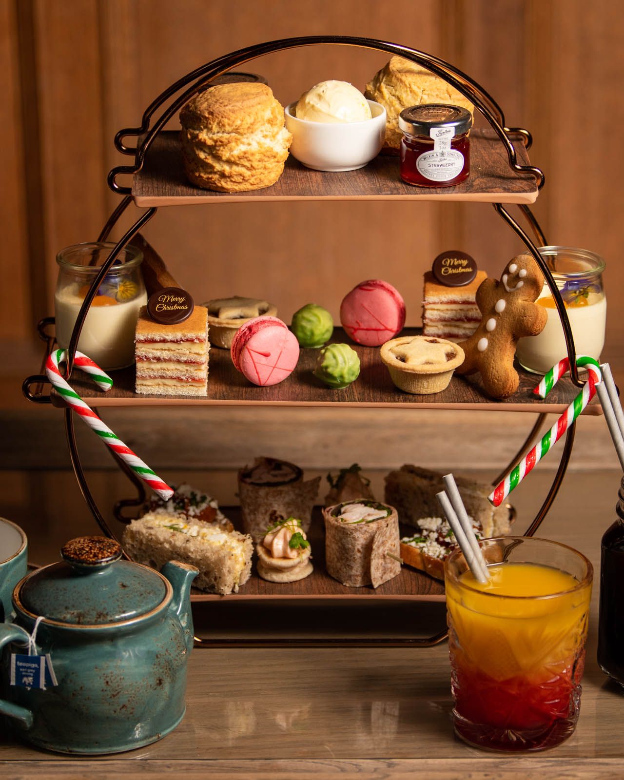 Festive afternoon tea set with scones, pastries, sandwiches, and festive drinks on a wooden table.