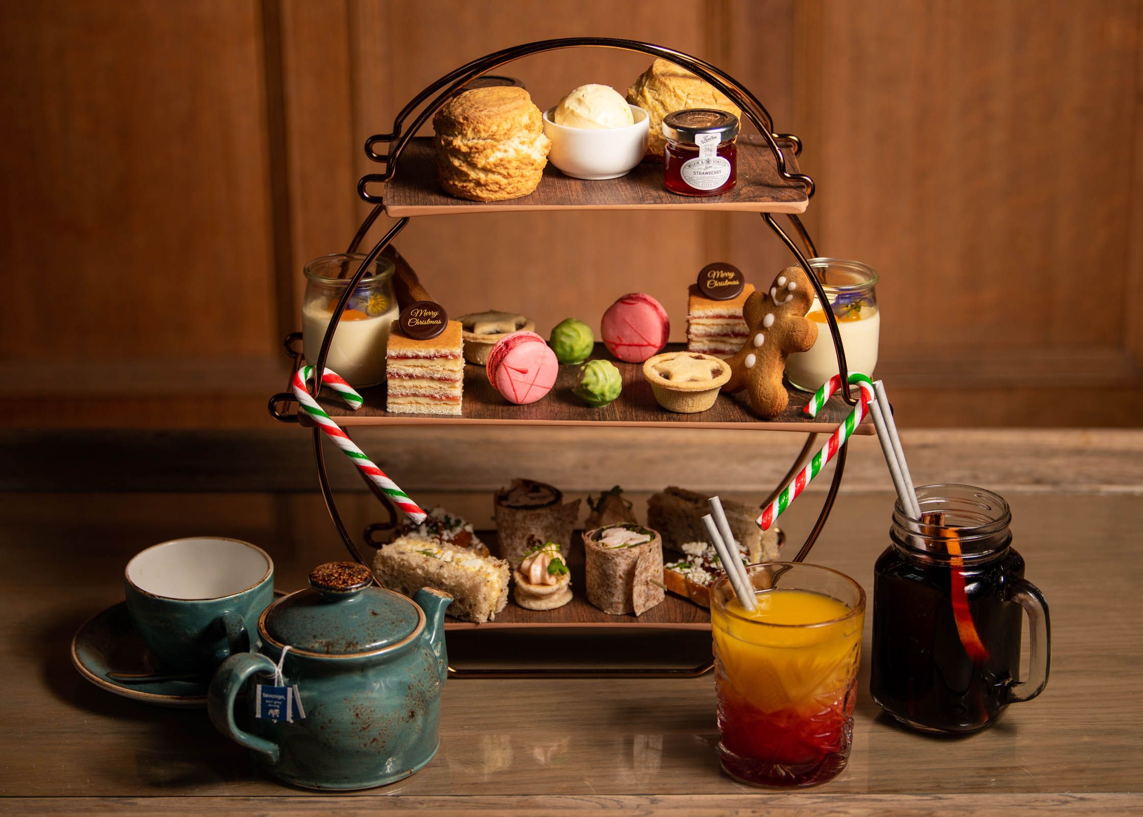 Festive afternoon tea set with scones, pastries, sandwiches, and festive drinks on a wooden table.