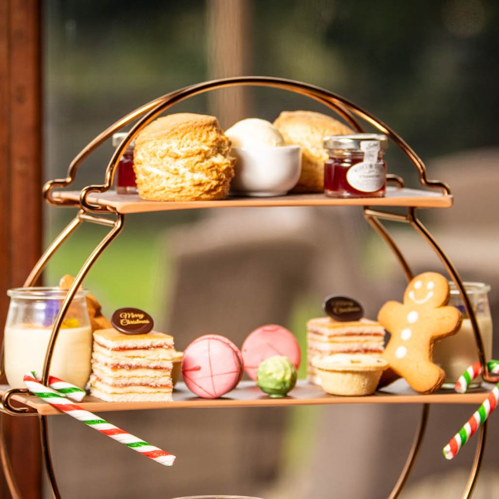 Festive afternoon tea set with teapot, cup, and a three-tiered stand of assorted pastries, sandwiches, and desserts.