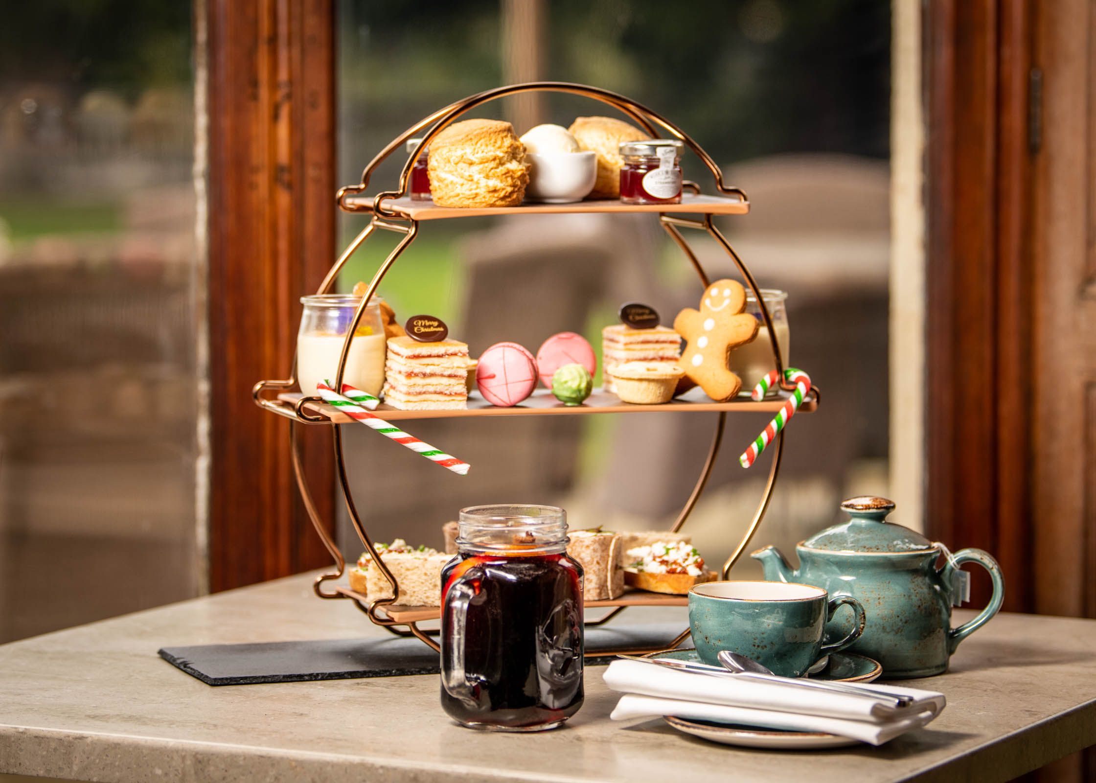 Festive afternoon tea set with teapot, cup, and a three-tiered stand of assorted pastries, sandwiches, and desserts.