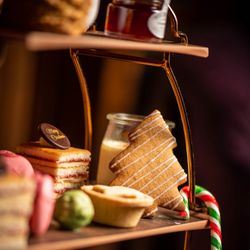 Festive afternoon tea tray with Christmas-themed treats including a tree-shaped cookie, candy cane, layered cake, and mince pie.